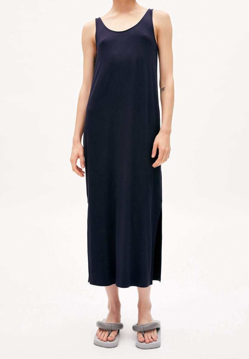 Marinblå ärmlös maxikjol tillverkad av mjukt tyg, med rund halsringning och sprund i sidorna. Matchas med grå klumpiga sandaler.