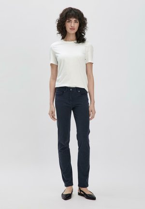 Witte t-shirt met korte mouwen, marineblauwe broek, aansluitend ontwerp, gladde textuur, subtiele stiksels, zwarte flats, staand tegen een neutrale achtergrond.
