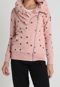 Felpa rosa con zip caratterizzata da pois grigi, cappuccio drappeggiato e polsini a coste. Realizzata in un tessuto morbido con una texture liscia.