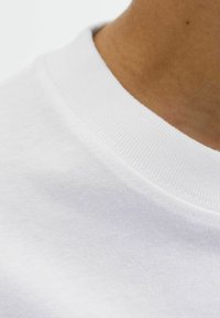 Guler de tricou alb din bumbac, prezentând o textură ribbată și un material neted. Detalii ale cusăturii vizibile pe linia gâtului.
