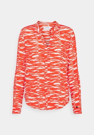 Chemise à manches longues boutonnée avec un motif abstrait de rayures zèbre en orange vif et blanc, col et poignets, posée à plat sur un fond blanc.