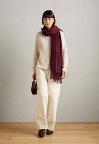 Pull beige à côtes, pantalon large crème, écharpe bourgogne foncé avec franges, chaussures marron et petit sac marron. Design minimaliste.