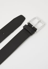 Curea din piele neagră cu o cataramă rectangulară argintie, textură netedă și un design cu vârf conic. Include princița cataramei și gauri pentru ajustare.