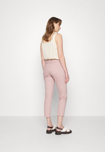 Jeans slim-fit cor rosa claro, combinados com uma t-shirt sem mangas beige e sandálias brancas de tiras. Apresenta uma cintura alta e bolsos traseiros.