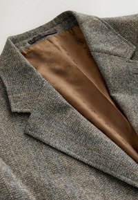 Herringbone-patterned blazer in gray with orange accents. Features a notched collar and smooth brown lining with a subtle floral pattern.