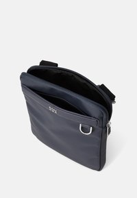 Bolso cruzado de nailon marino con cremallera superior, que cuenta con un bolsillo delantero, herrajes en plata y una correa ajustable. El interior está forrado con tela negra.