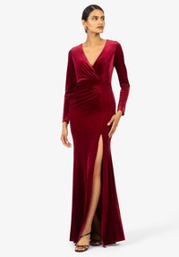 Langes bordeauxfarbenes Samtkleid mit tiefem V-Ausschnitt, langen Ärmeln, gerafftem Stoff in der Taille und einem seitlichen Schlitz bis zum Oberschenkel.