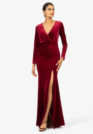 Lungo vestito di velluto bordeaux con scollatura a V profonda, maniche lunghe, tessuto arricciato in vita e una fessura laterale alta fino alla coscia.