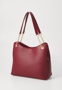 Sac à main en cuir rouge à texture granuleuse, avec des double poignées et des accents en chaîne dorée. Il présente une forme décontractée et une poche zippée sur le côté pour un rangement supplémentaire.
