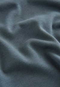 Niebiesko-szary bawełniany materiał o miękkiej teksturze, z delikatnymi fałdami i zmarszczkami, podkreślającymi jego elastyczność i układ.