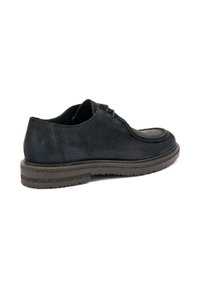 Zapato negro de ante con cordones y suela texturizada, capturado desde un ángulo lateral que resalta su diseño elegante y los detalles de costura.