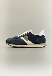 Baskets de sport bleu marine et blanches avec empiècements en suède et en mesh, semelle crème, lacets blancs et pièce marron sur le côté, présentées de profil.