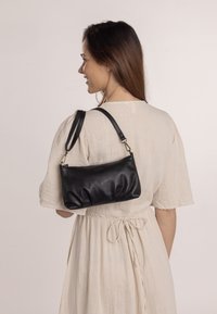 Zwarte leren handtas met een zachte, geplooide textuur, voorzien van een korte schouderband en subtiele gouden hardware accenten.