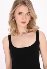Schwarzes Tanktop mit quadratischem Ausschnitt. Das Modell trägt lavendelfarbene Creolen und eine Perlenkette mit lila und weißen Akzenten.