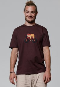 Bordeaux katoenen t-shirt met een kleurrijke bedrukte afbeelding van een personage op een fiets. Korte mouwen en een ontspannen pasvorm.