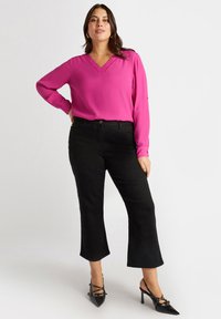 Blusa fucsia con scollo a V e maniche lunghe abbinata a pantaloni neri a gamba svasata alla caviglia e tacchi a spillo neri con borchie.
