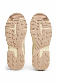 Semelle de sneaker beige avec un motif de traction texturé, présentant des rainures et des reliefs prononcés, des sections lisses et une marque de logo.