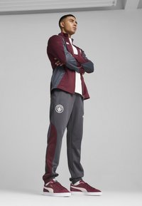 Bordeaux og grå atletisk jakke med lynlås og logo, parret med grå bukser med logo og farveaccent; bordeaux sneakers.