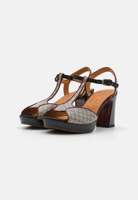Heeled sandals with a patterned upper in white and black, open toe, and black patent leather accents. Adjustable ankle strap.