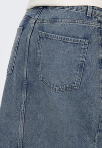 Denim krilo s svetlo modrim pranjem, dolžina do kolen, in zadnjim žepom klasične pravokotne oblike ter prišitimi detajli.