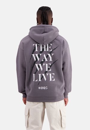 Gray hoodie with a large black and white graphic reading "THE WAY WE LIVE" on the back, featuring claw-like accents. Fabric appears soft.