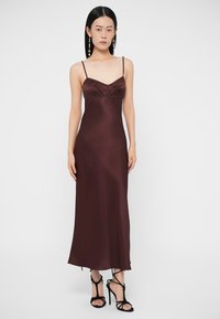 Saténové šaty na ramienka v bordovej farbe s tenkými ramienkami, priliehavým živôtikom a splývavou sukňou. Hladká textúra a jemný lesk. Čierne sandále na opätku s remienkami.