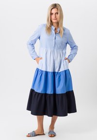 Knoopsluiting, lange mouwen jurk met gelaagd ontwerp in lichtblauw, donkerblauw en marineblauw. Bevat strepen, zakken en een vloeiende silhouet.