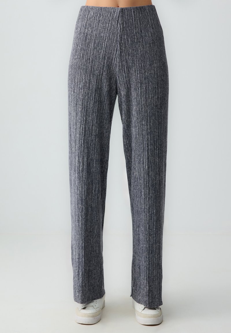 Grijze, ribbelige wijde broek met hoge taille, gemaakt van zacht materiaal, met een subtiele textuur en een rechte pasvorm, gecombineerd met witte sneakers.