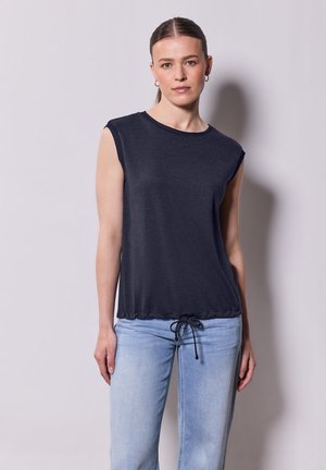Top sin mangas de color gris oscuro con cuello redondo, cordón en el dobladillo y tela suave. Combinado con unos vaqueros de mezclilla azul claro.