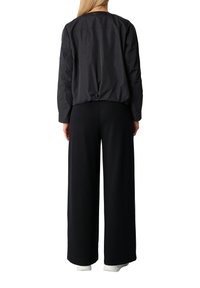 Giubbotto bomber nero realizzato in tessuto leggero e liscio, con vita arricciata e maniche lunghe, abbinato a pantaloni neri a gamba larga.