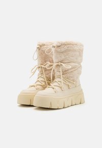 Beige winterlaarzen hebben een pluizige bont bovenkant, ronde neus en een chunky rubberen zool met zigzagdetails. Inclusief veters en een verstelbare trekkoord.