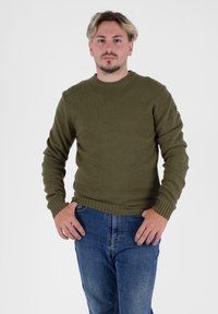 Oliwkowy, dzianinowy sweter o prążkowanej teksturze, z okrągłym dekoltem i długimi rękawami; zestawiony z niebieskimi dżinsami. Prosty fason i dopasowany krój.