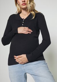 Blusa de manga longa preta com textura canelada, colarinho e fileira de botões, apresentando um corte justo na cintura e um tecido suave. Combinada com um jeans claro.