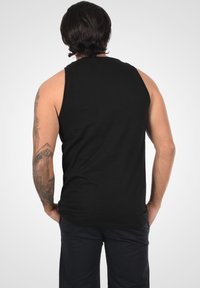 Sort ærmeløs tank top lavet af bomuld; har en afslappet pasform og subtil tekstur. Bagview viser en glat finish uden synlige mønstre.