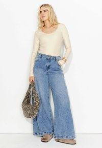 Un haut beige à manches longues avec une bordure en dentelle, un jean large taille haute bleu, des mules compensées marron clair et un sac à imprimé léopard marron.