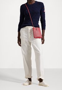 Maglione a trecce blu navy, pantaloni larghi crema, sneakers bianche e una piccola borsa a tracolla rossa. Materiali testurizzati, design casual.