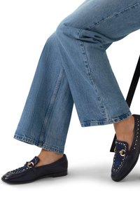 Marine loafers met een gestructureerde afwerking, voorzien van gouden studs en een decoratieve hardwareaccent. Gecombineerd met lichtblauwe wijdvallende jeans.