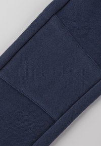 Hintergrundstoff-Zubehör in Marineblau mit einer strukturierten Oberfläche und einem geometrischen Paneeldesign. Merkmale saubere Nähte und einen engen Sitz.