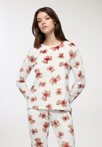 Completo pigiama a maniche lunghe in bianco con motivo orsetto in marrone e rosso. Tessuto morbido, vestibilità casual; la parte superiore ha scollo a girocollo e i pantaloni hanno una vita elasticizzata.