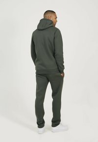 Sweat à capuche vert olive et joggings assortis en tissu doux et texturé. Comprend une capuche, des poches latérales et des baskets blanches. Design minimaliste.