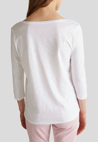 Witte, lichtgewicht longsleeve top met een losse halslijn en driekwartmouwen, met een subtiele textuur en logo-detail op de rug.