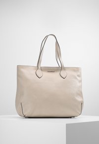 Sac cabas en cuir beige avec double anses d'épaule, forme arrondie, texture subtile et accents noirs le long des bords et des anses.