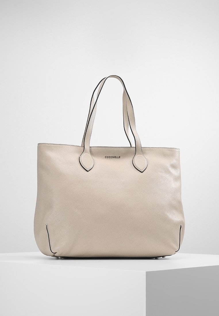 Sac cabas en cuir beige avec double anses d'épaule, forme arrondie, texture subtile et accents noirs le long des bords et des anses.