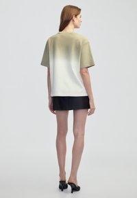 T-shirt à manches courtes dans un dégradé d'olive se fondant en blanc, fabriqué en tissu doux. Associé à une mini jupe noire, mettant en valeur une silhouette élégante.