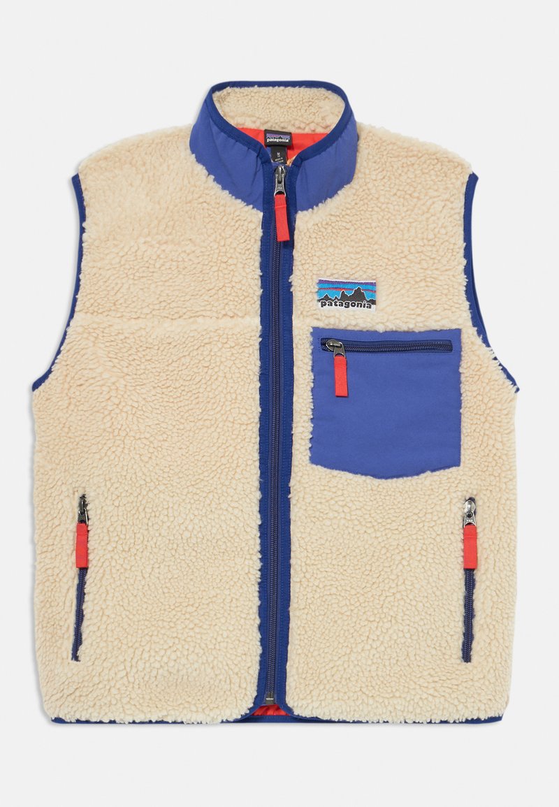 Γιλέκο από teddy fleece σε μπεζ χρώμα με μπλε μπροστινό πάνελ, διαθέτοντας μια τσέπη στο στήθος με φερμουάρ και δύο πλαινές τσέπες. Οι λαβές του φερμουάρ είναι κόκκινες.