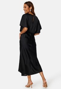 Zwarte satijnen jurk met een losse, vloeiende uitstraling, korte mouwen en een sleutelgaatje aan de achterkant. Gladde textuur met een halflange zoom.