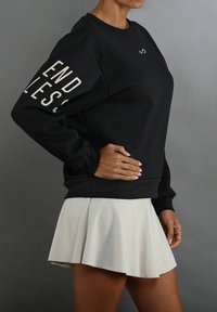 Sudadera negra con el texto "ENDLESS" en la manga, combinada con una falda plisada ligera y acampanada. Presenta un cuello redondo y mangas largas.