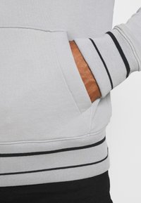 Sudadera gris con puños de canalé a rayas en blanco y negro. Presenta un bolsillo frontal con una textura suave y costuras estructuradas.