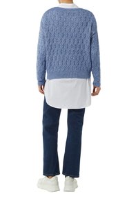 Lichtblauwe gebreide trui met een gestructureerd ruitpatroon, geribbelde manchetten en zoom, gedragen over een wit shirt, gecombineerd met donkere denim en witte sneakers.