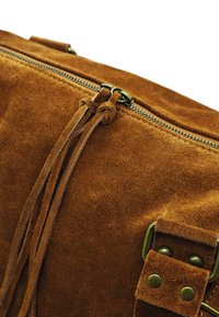 Sac en suédine brun avec fermeture éclair, doté de pampilles en cuir et d'accents en métal. Texture douce et forme rectangulaire, adapté à un usage décontracté.